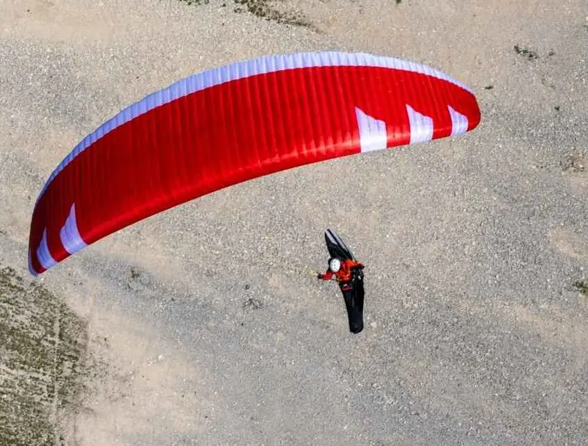 Red paraglider glides over rocky terrain in aerial perspective