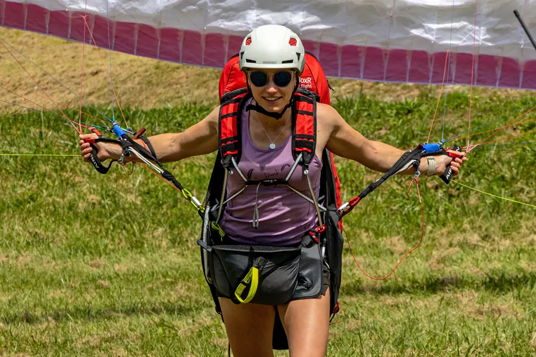 Female paraglider pilot walking with harness after landing