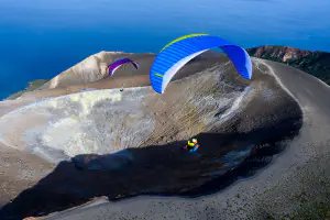 Two paragliders soar above a volcanic crater by the sea
