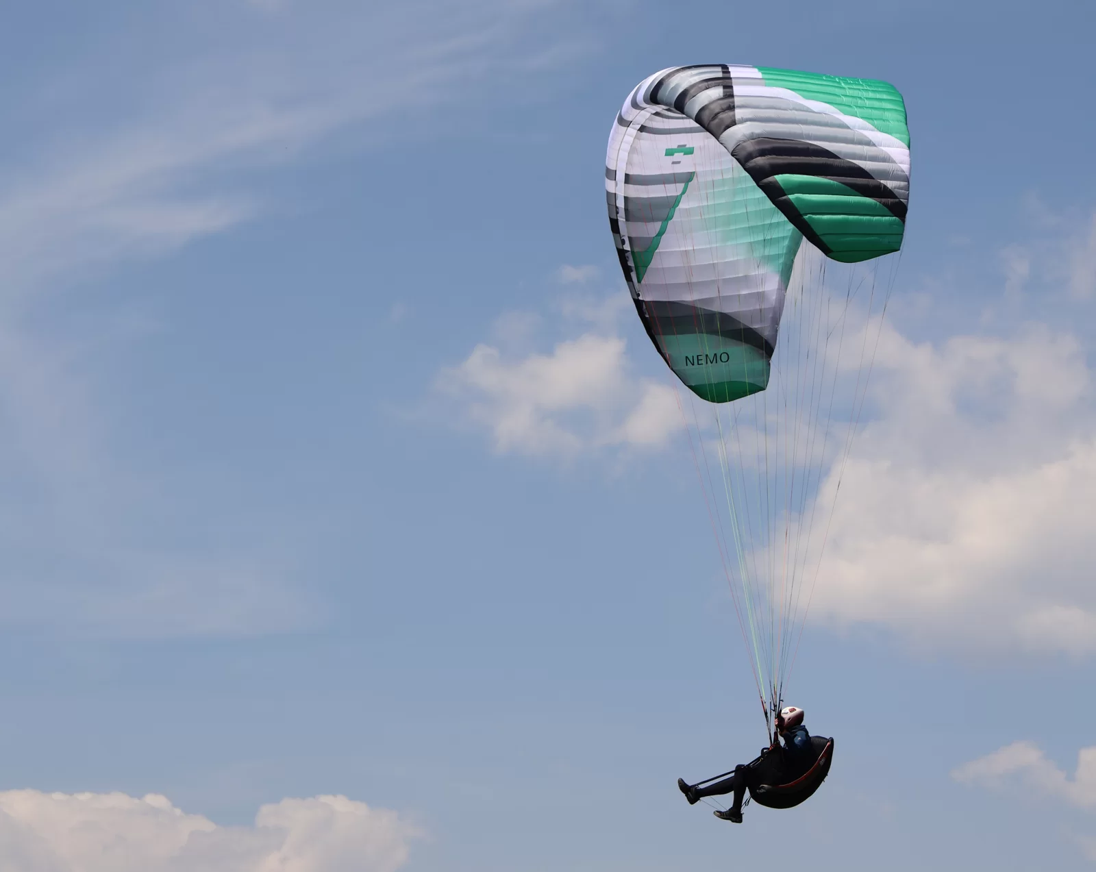 Green, white and black Nemo 5 paraglider flying against a clear blue sky above a rocky landscape