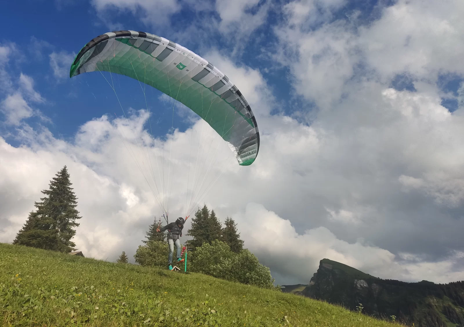 Green and white Nemo 5 paraglider canopy viewed from below against a partly cloudy sky
