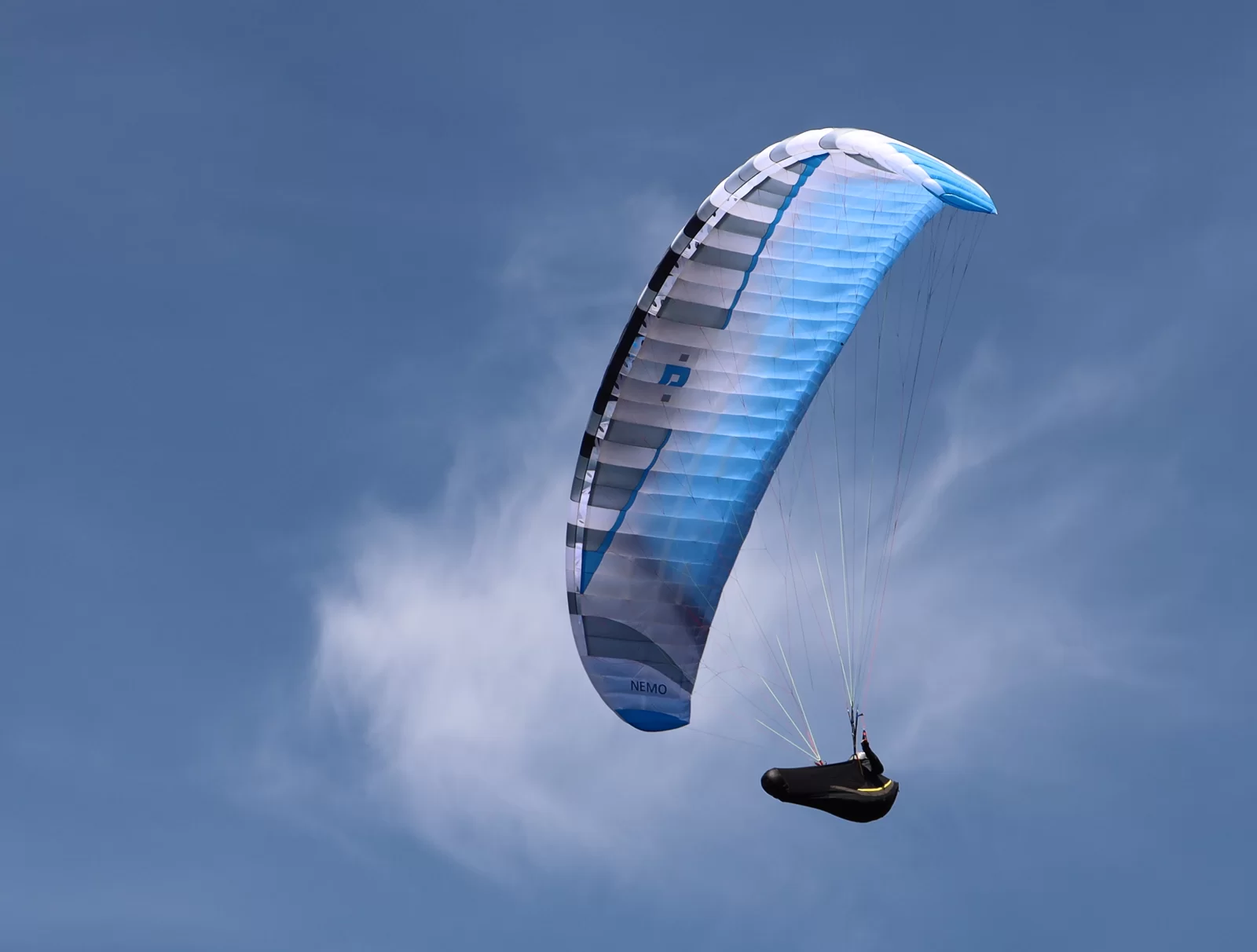 Blue and white Nemo 5 paraglider wing soaring through the sky with its curved canopy fully inflated