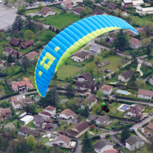 Blue and green Halo paraglider flying above a residential area surrounded by green fields