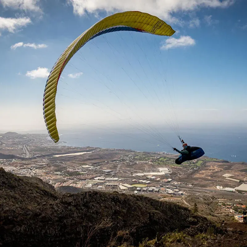 Yellow and dark blue Airdesign Hero Xped paraglider flying above a rugged mountain slope