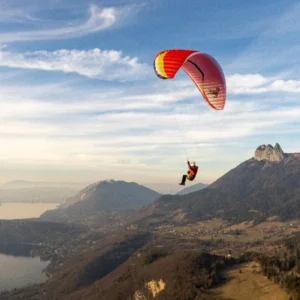 Red and yellow Airdesign Loco paraglider flying above a mountain slope under a partly cloudy sky