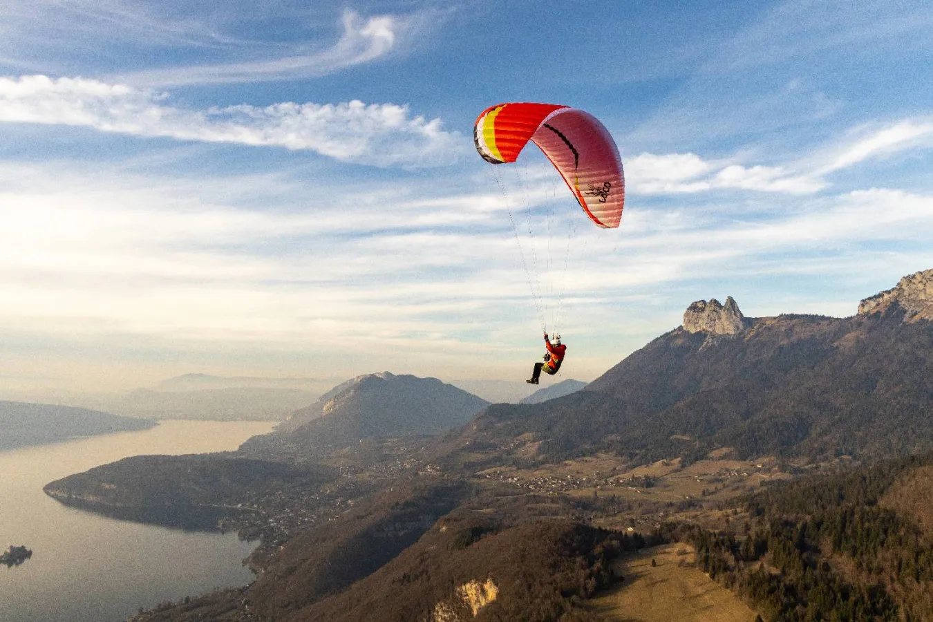Red and yellow Airdesign Loco paraglider flying above a mountain slope under a partly cloudy sky
