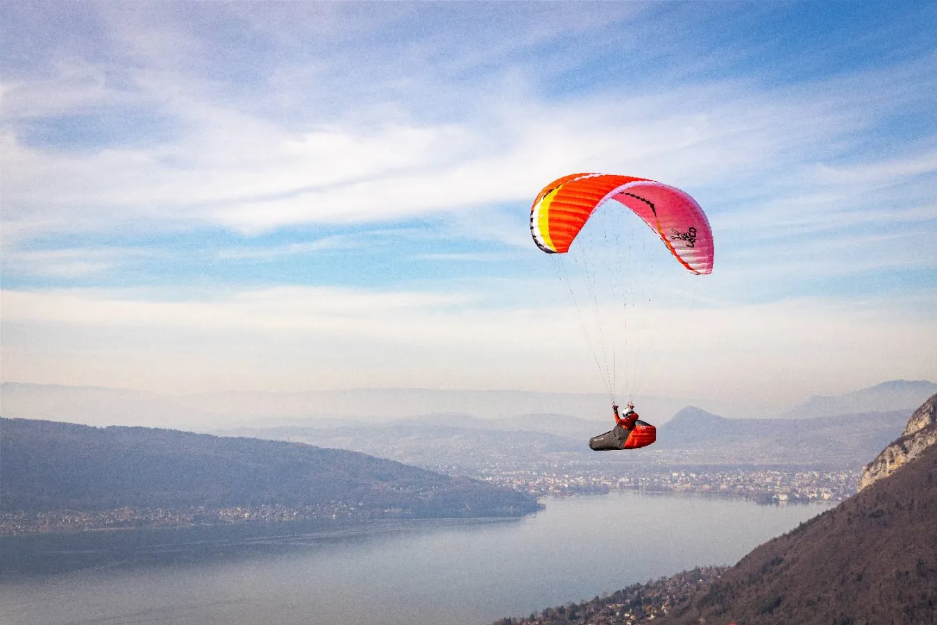 Red and yellow Airdesign Loco paraglider flying across an open sky above a distant mountain landscape