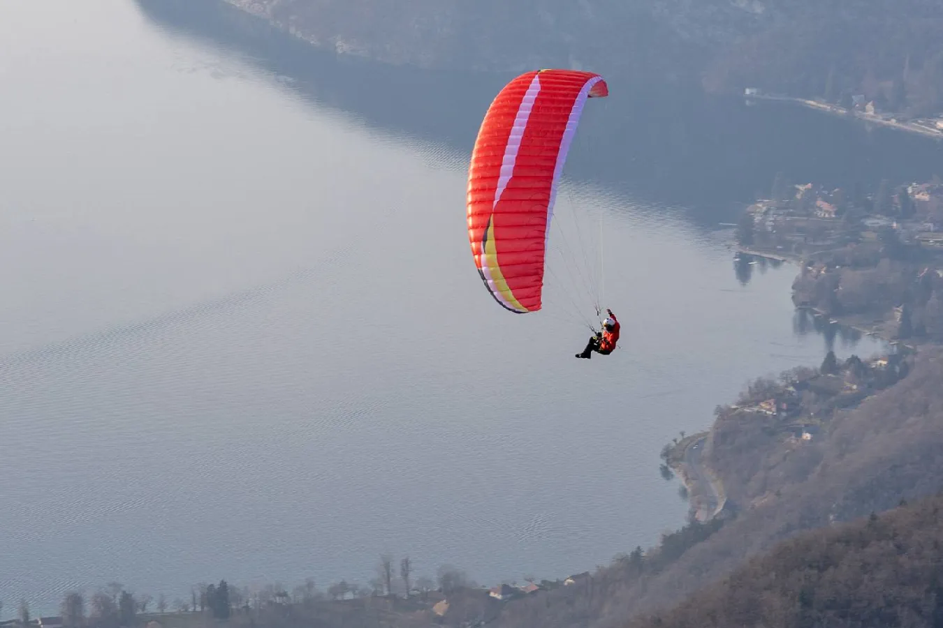Red Airdesign Loco paraglider canopy soaring against a grey and blue cloudy sky