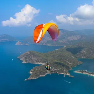 Orange and yellow Airdesign Ride 4 tandem paraglider flying above a blue coastal landscape