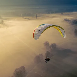 Yellow and white tandem paraglider flying low over a wide sandy beach beneath a cloudy sky